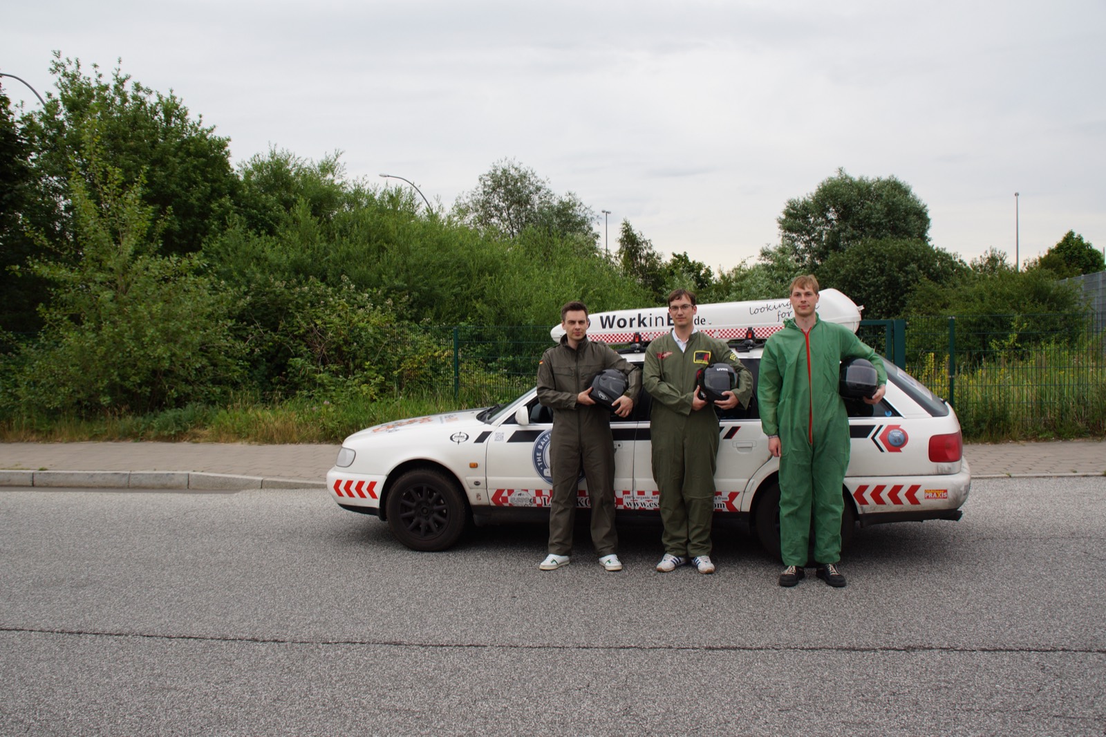 Drei Teamkollegen in Rennoveralls vor ihrem Auto